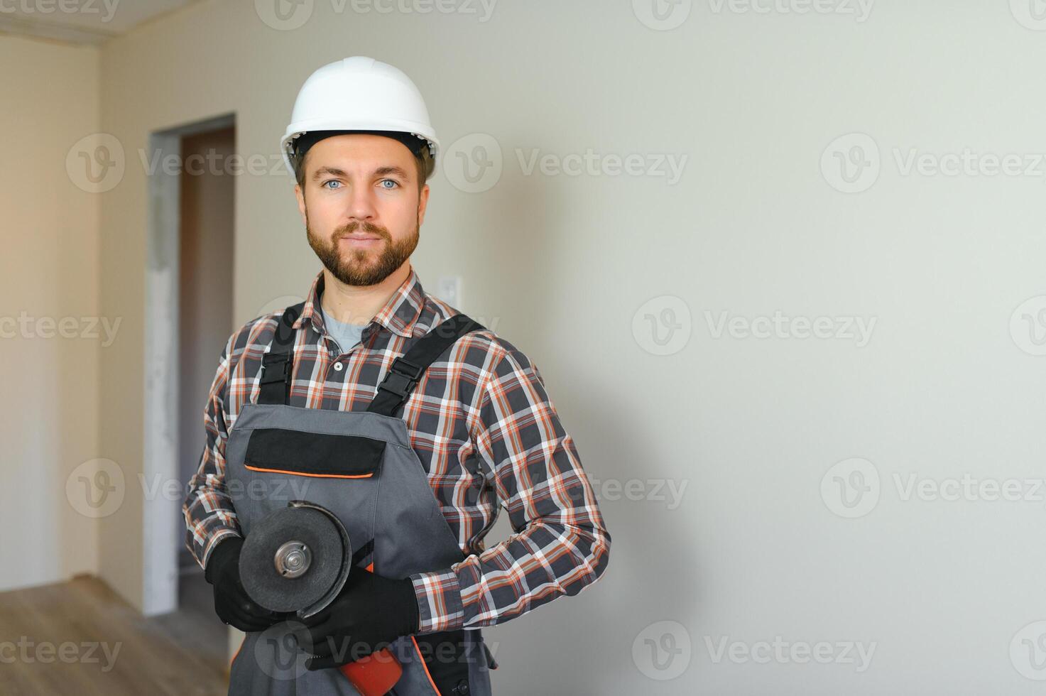 porträtt av positiv, stilig ung manlig byggare medan arbetssätt på konstruktion webbplats. foto