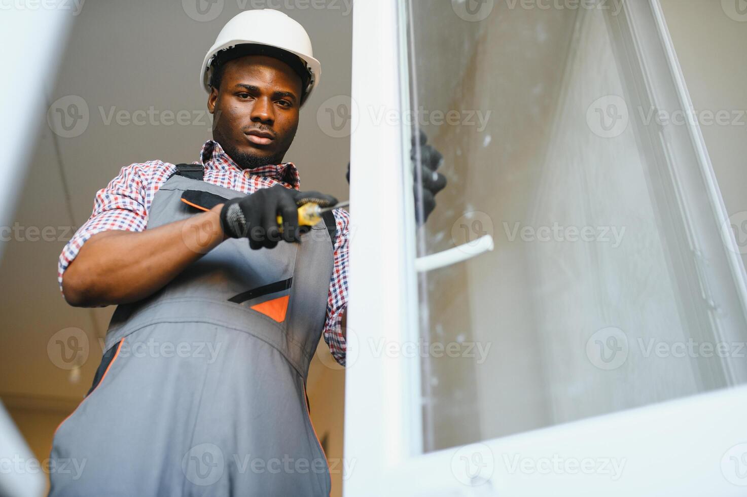 ung afrikansk hantlangare i enhetlig fixering glas fönster med skruvmejsel foto