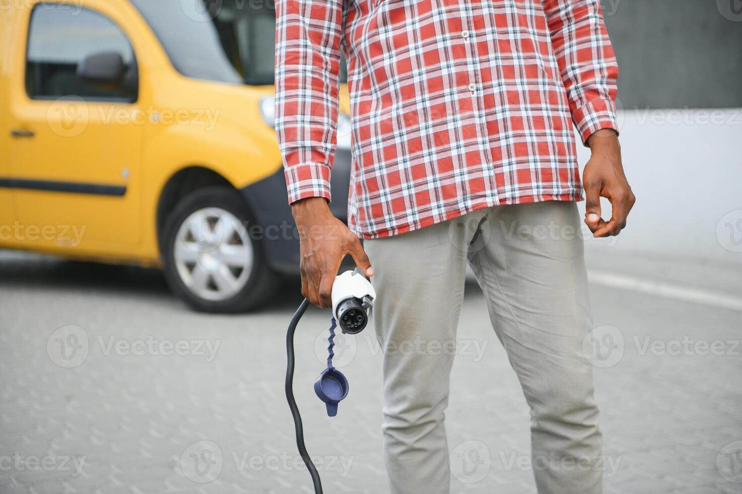 afrikansk man innehav avgift kabel- i på hand stående nära elektrisk bil foto