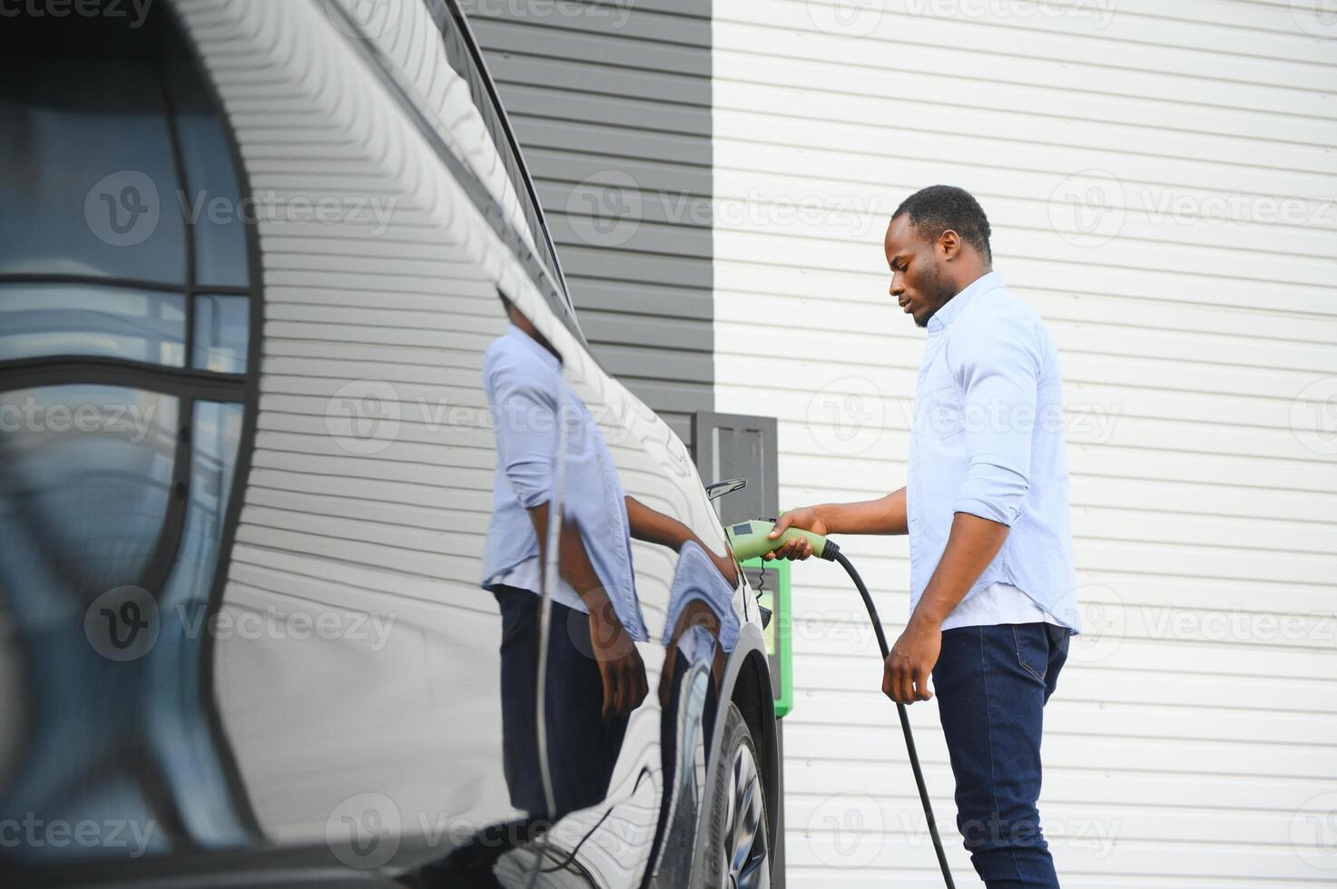 allvarlig afrikansk man innehav avgift kabel- i på hand, stående nära lyx elektrisk bil. foto