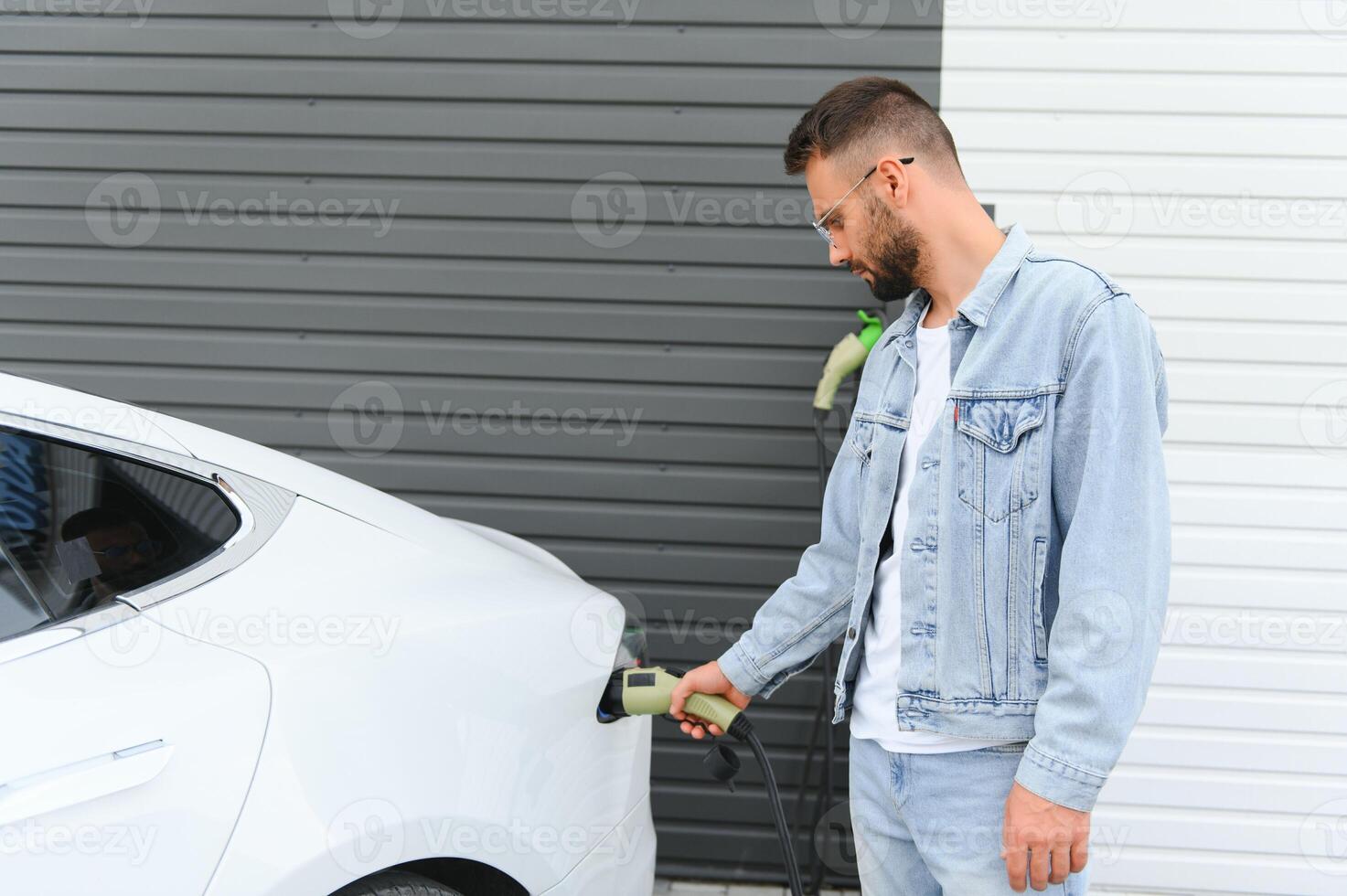 man innehav kraft laddning kabel- för elektrisk bil i utomhus- bil parkera. och han s gående till ansluta de bil till de laddning station i de parkering massa nära de handla Centrum. foto