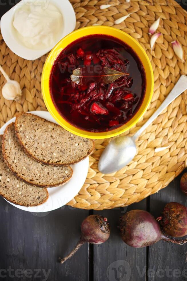 röd traditionell ryska och ukrainsk borscht eller rödbeta soppa med sur grädde, vitlök och aromer i en gul keramisk kopp på korg- bordstablett bakgrund. foto