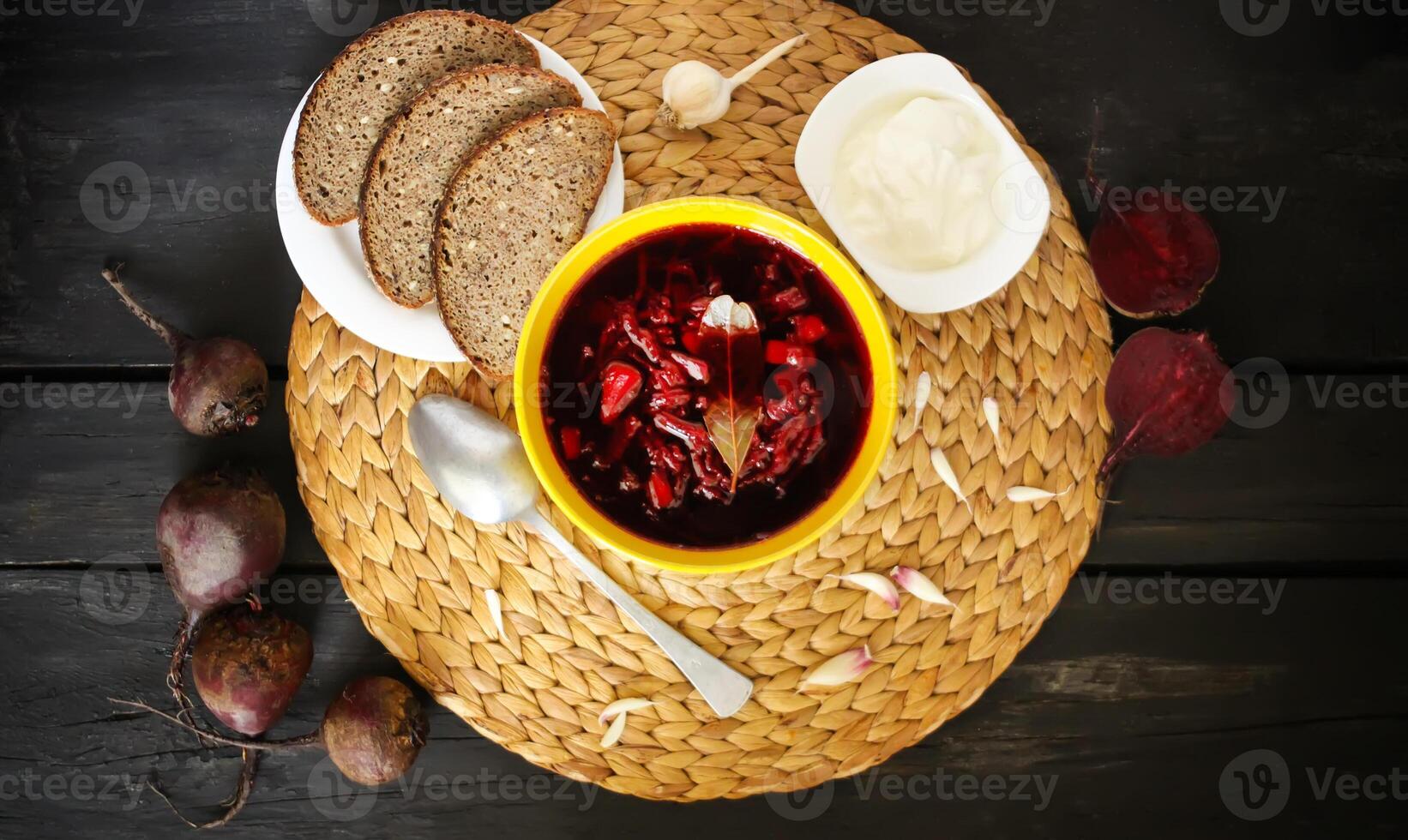 röd traditionell ryska och ukrainsk borscht eller rödbeta soppa med sur grädde, vitlök och aromer i en gul keramisk kopp på korg- bordstablett bakgrund. foto