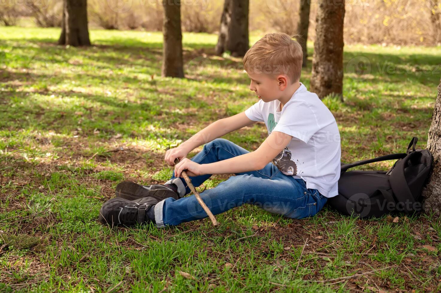 en pojke med en pinne sitter på de gräs i en vår parkera foto