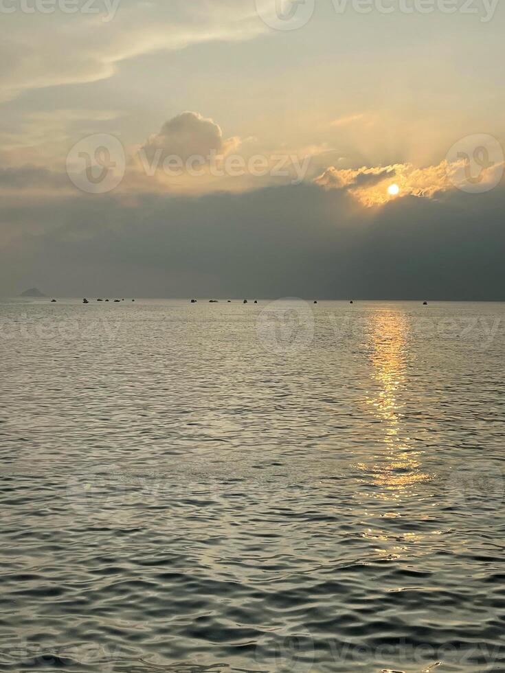 skön solnedgång på de hav, de Sol uppsättningar Bakom en stor moln liggande på de vatten foto