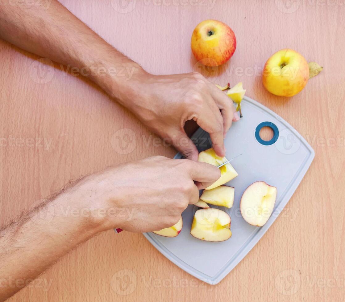 stänga upp manlig händer skära ett äpple in i skivor. topp se av framställning frukt över kök tabell. foto