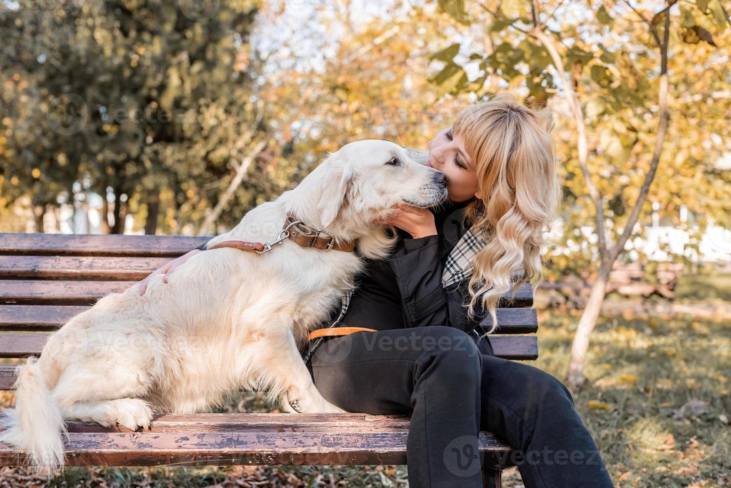 blond kaukasisk kvinna sitter med sin gyllene labrador retrieverhund på bänken i parken foto