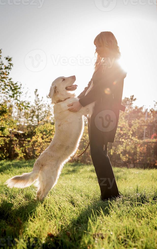 vacker kaukasisk kvinna som leker med sin gyllene labrador retrieverhund i en park i solnedgången foto