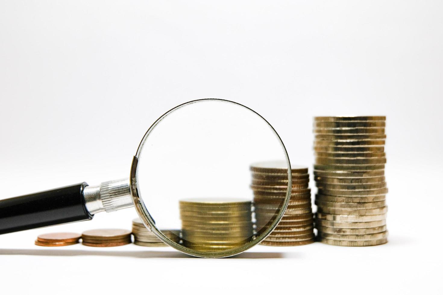 stapla mynt pengar växer och ökar med förstoringsglas på vit bakgrund för sparande och affärsinvesteringskoncept. foto