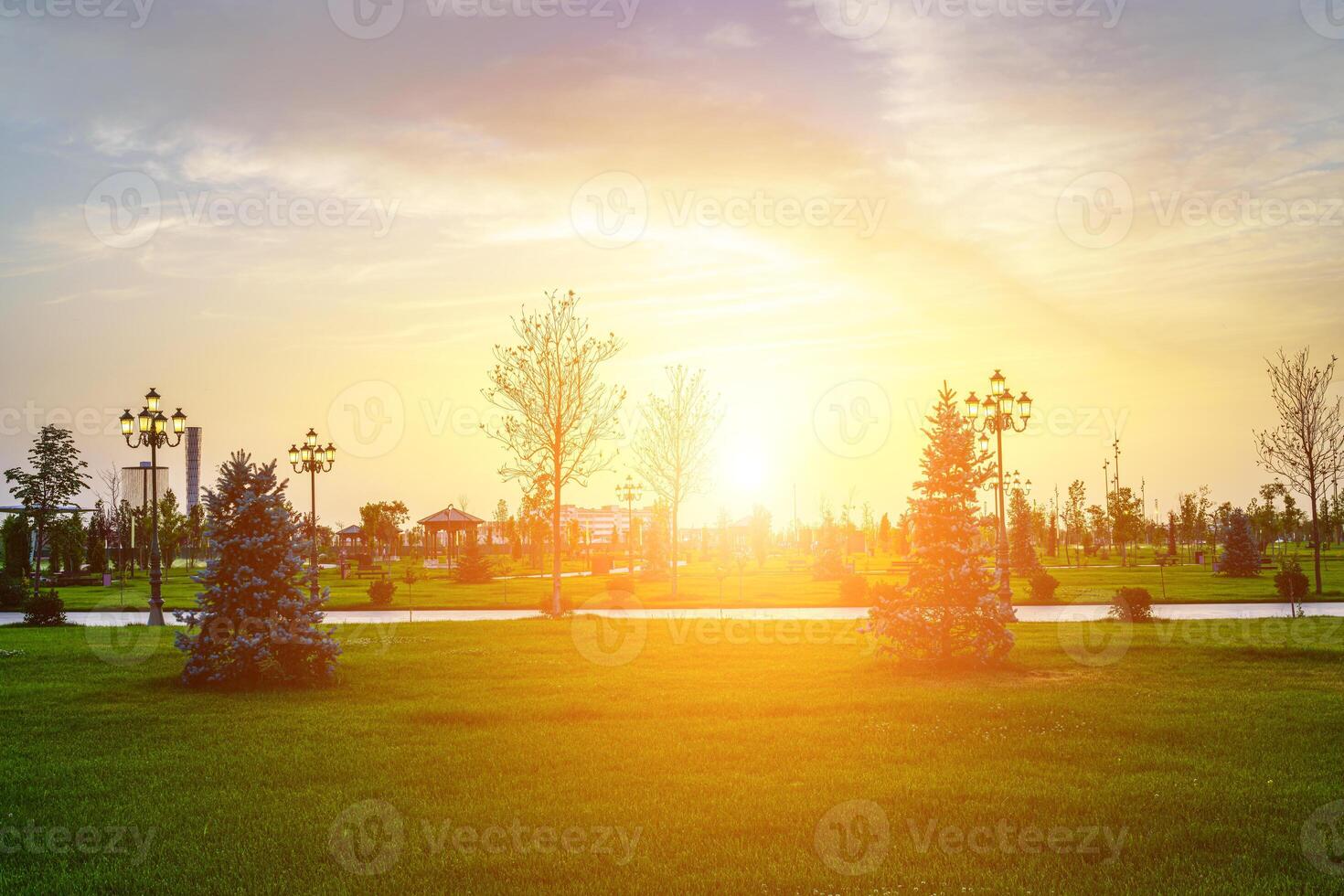 stad parkera i tidigt sommar eller vår med lyktor, ung grön gräsmatta, träd och dramatisk molnig himmel på en solnedgång eller soluppgång. foto