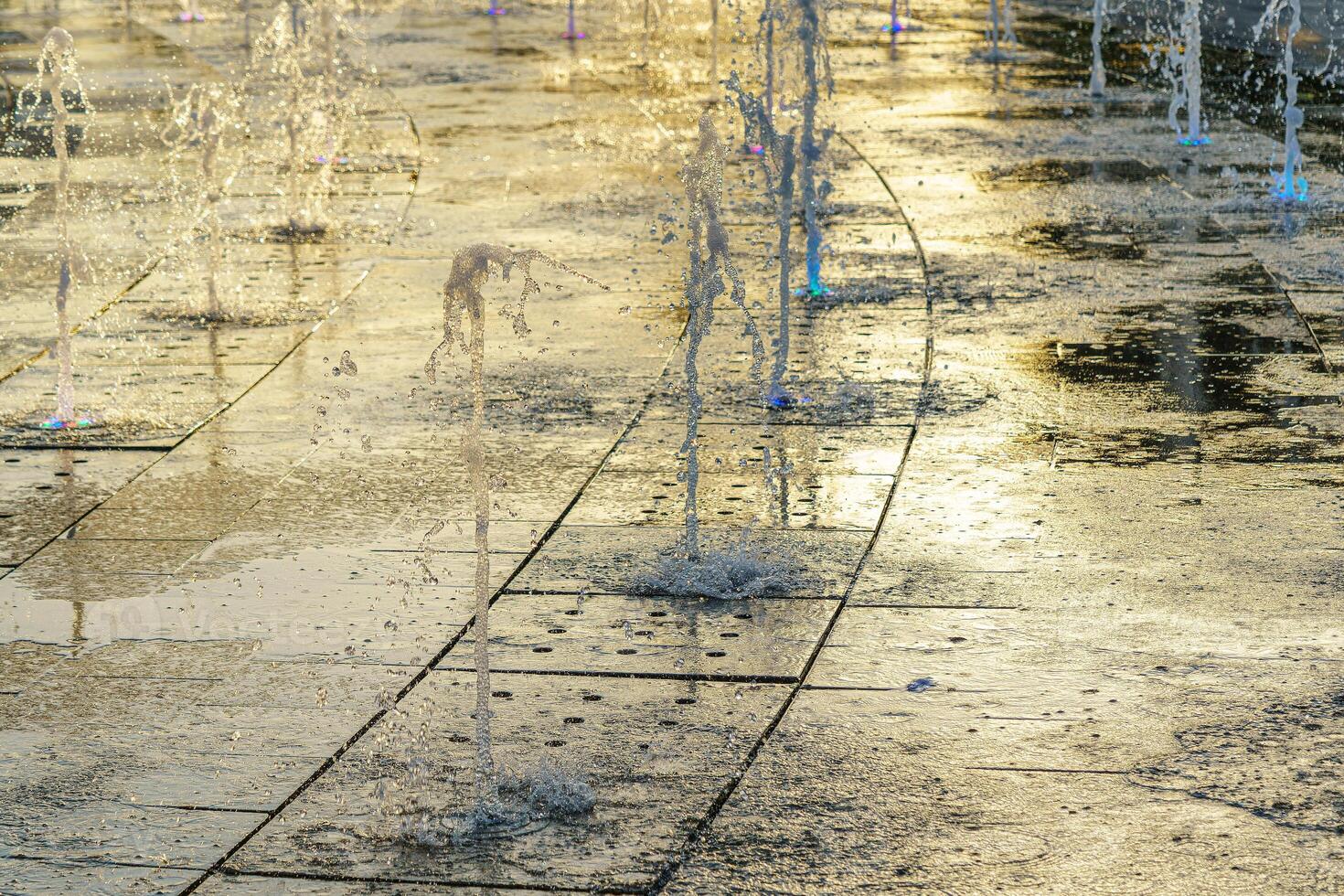 små fontäner på de trottoar, upplyst förbi solljus på solnedgång eller soluppgång på sommartid. foto
