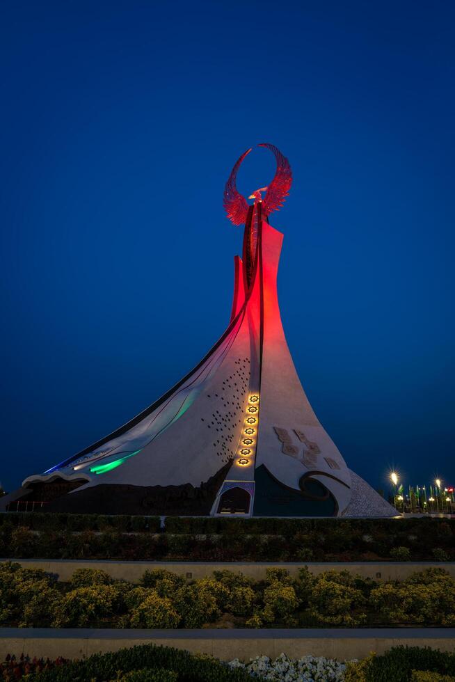 uzbekistan, Tasjkent - Maj 5, 2023 upplyst monument av oberoende i de form av en stele med en humo fågel, fontäner och vinka flaggor i de ny uzbekistan parkera på nattetid. foto