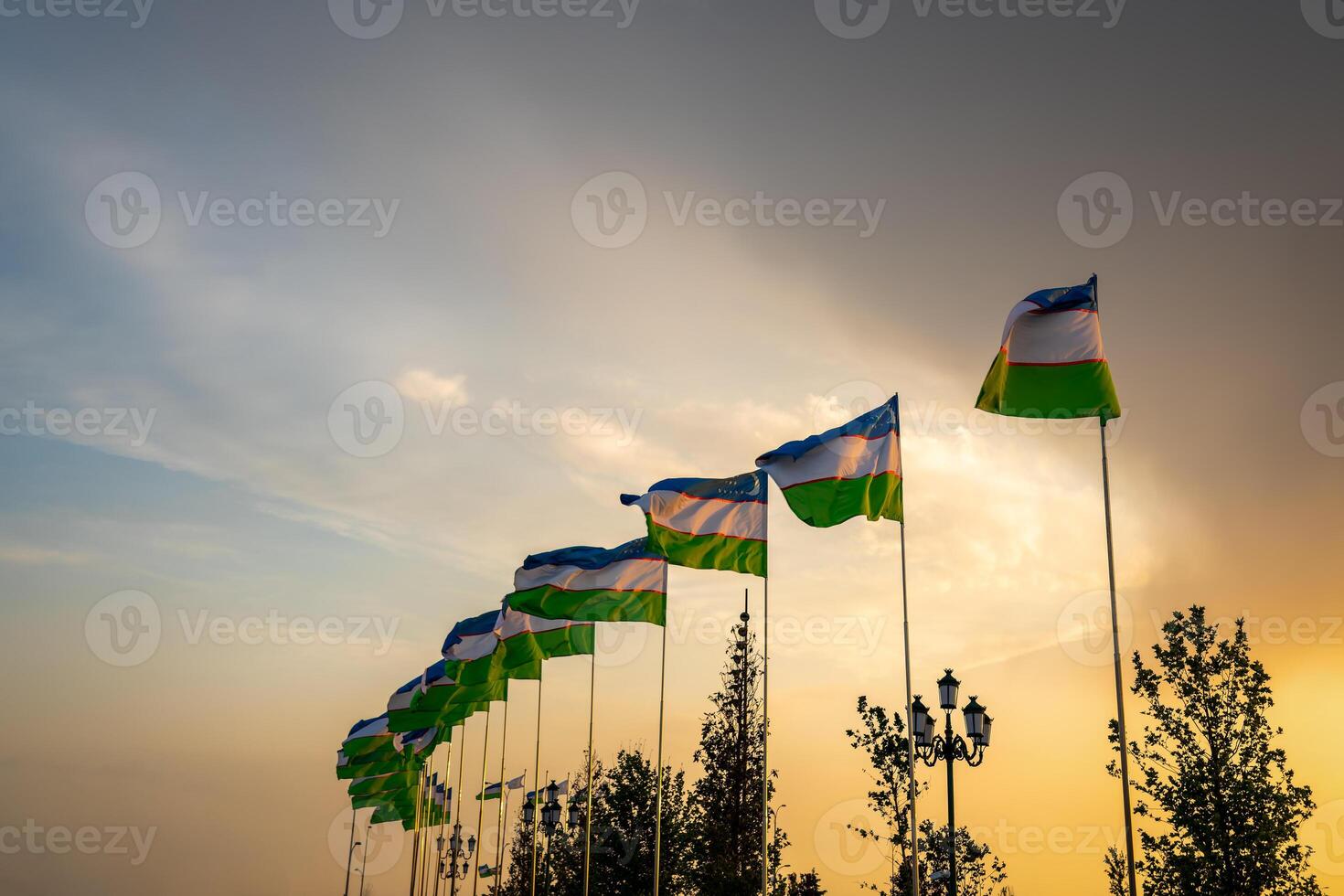 flaggor av uzbekistan vinka på en solnedgång eller soluppgång dramatisk himmel bakgrund. foto