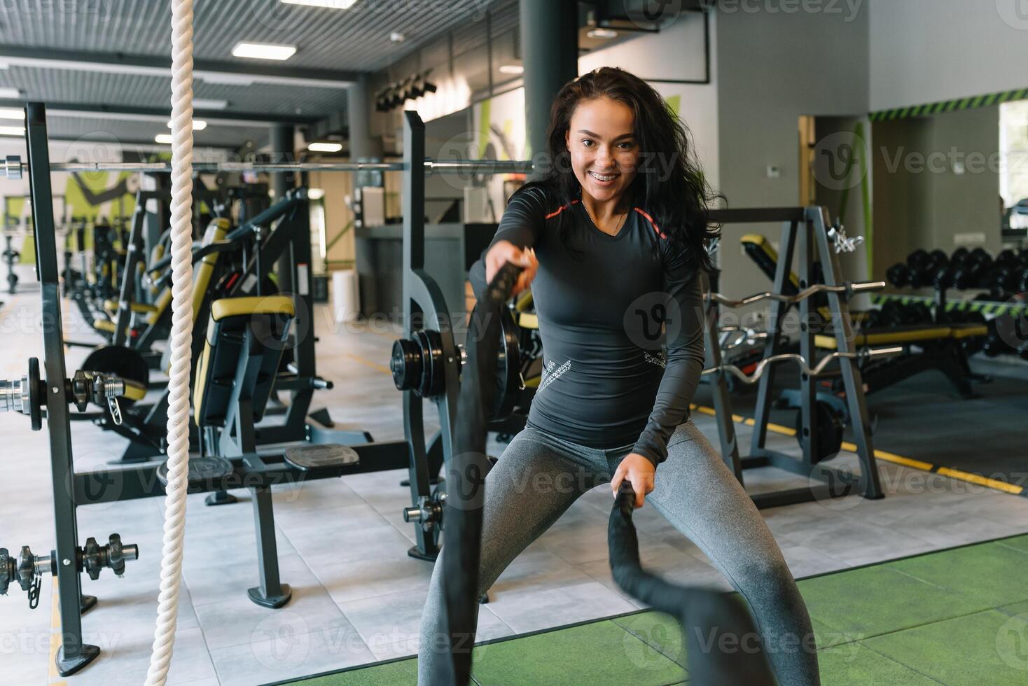 Söt latinamerikan ung kvinna håller på med några crossfit övningar med en rep på en Gym. foto