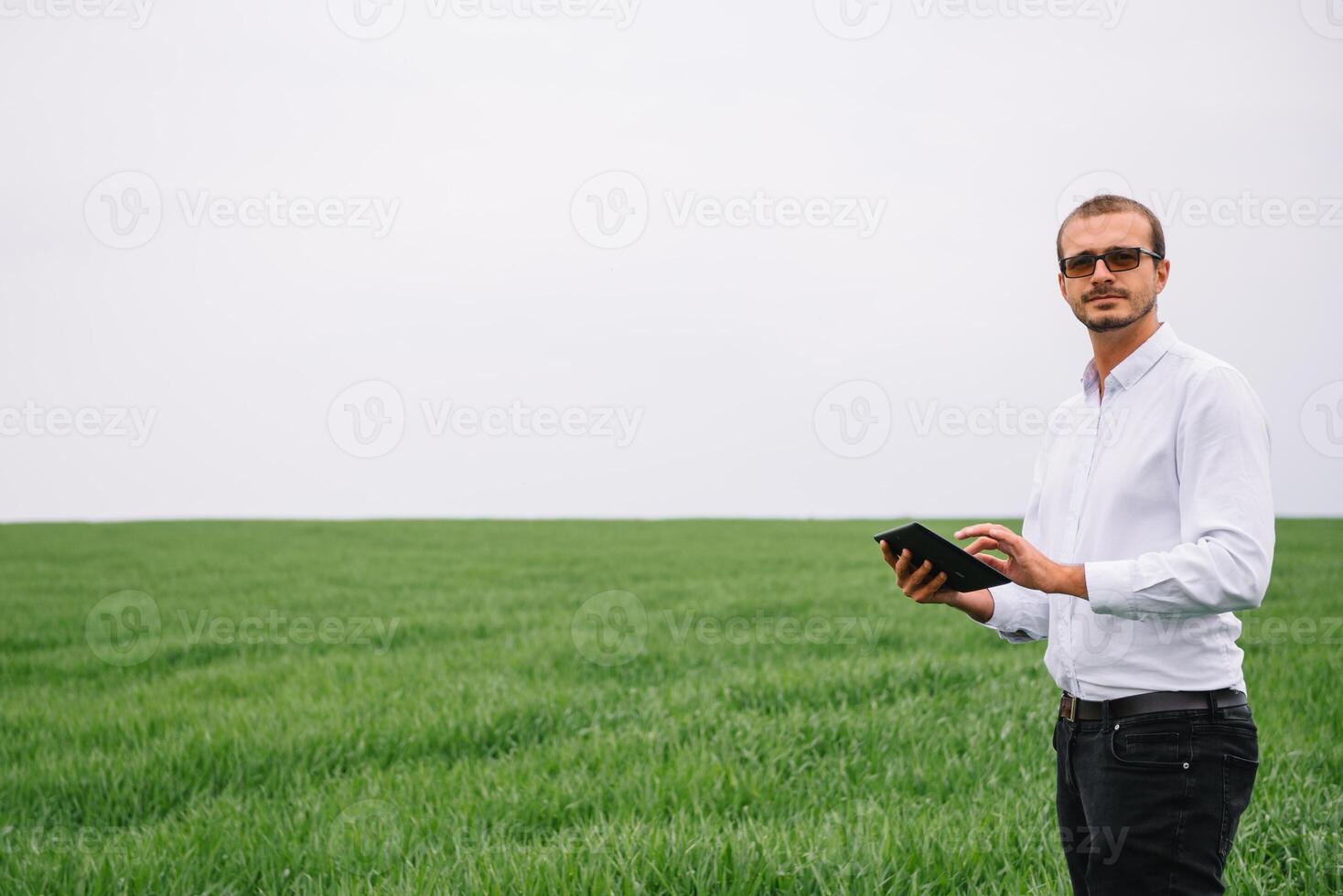 ung agronom innehar läsplatta Rör vaddera dator i grön vete fält. jordbruksnäringen begrepp. jordbruks ingenjör stående i en vete fält med en läsplatta i sommar foto