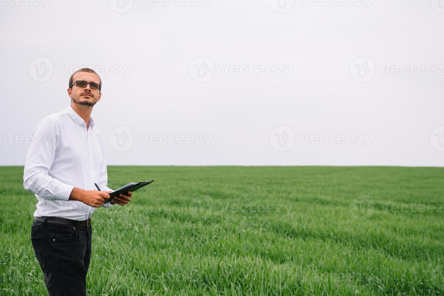 ung stilig agronom, lantbruk ingenjör stående i grön vete fält med läsplatta i händer i tidigt sommar. jordbruksnäringen begrepp. foto