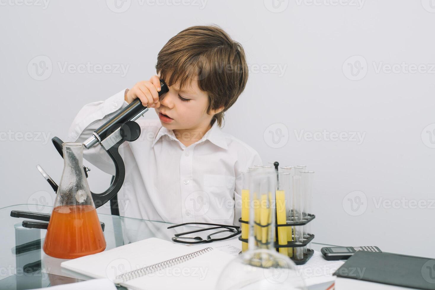 de pojke med en mikroskop och olika färgrik kolvar på en vit bakgrund. en pojke håller på med experiment i de laboratorium. explosion i de laboratorium. vetenskap och utbildning. foto