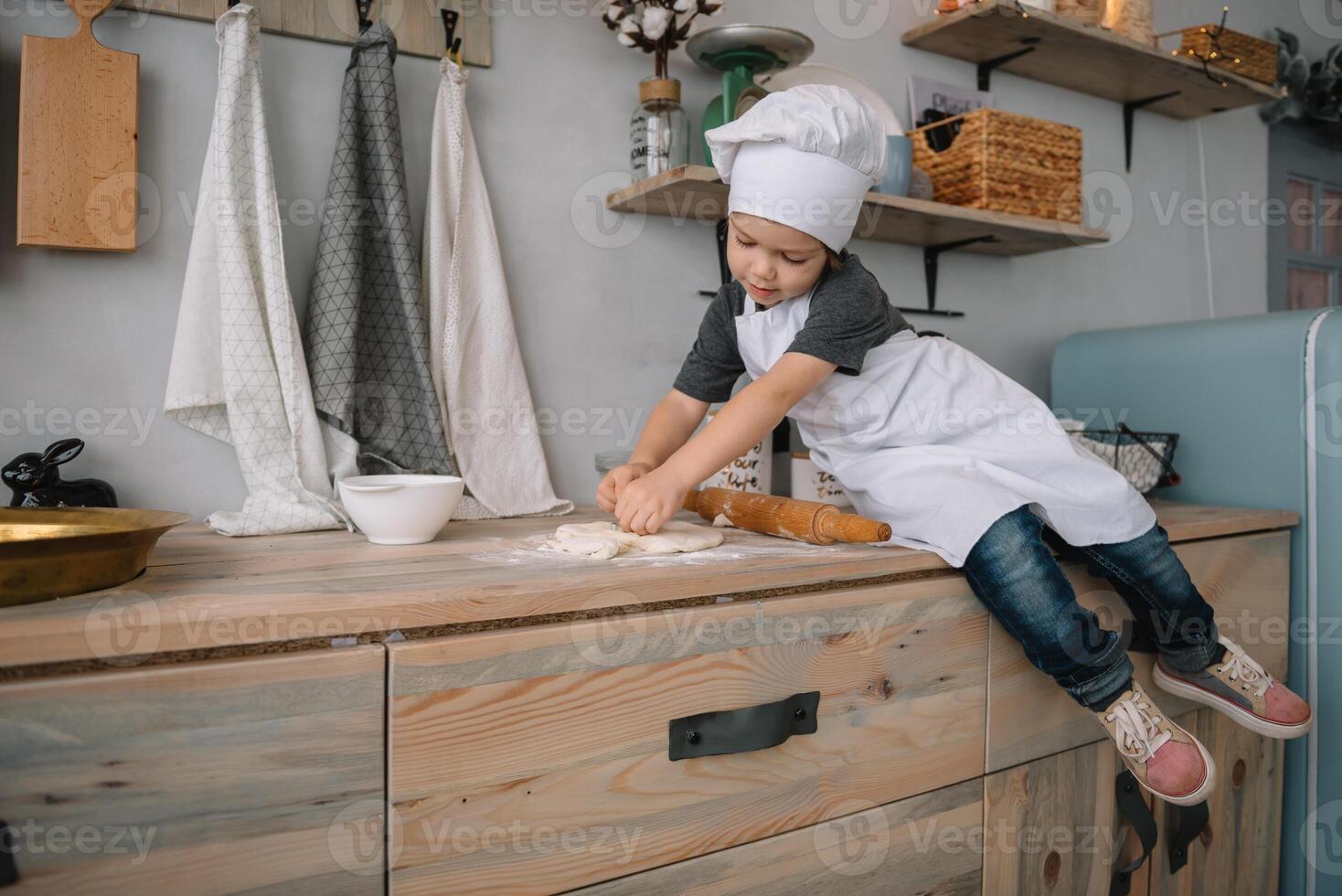 ung Lycklig mamma och henne bebis laga mat småkakor på Hem i de kök. jul hemlagad pepparkaka. söt pojke med mor i vit enhetlig och hatt kokta choklad småkakor foto