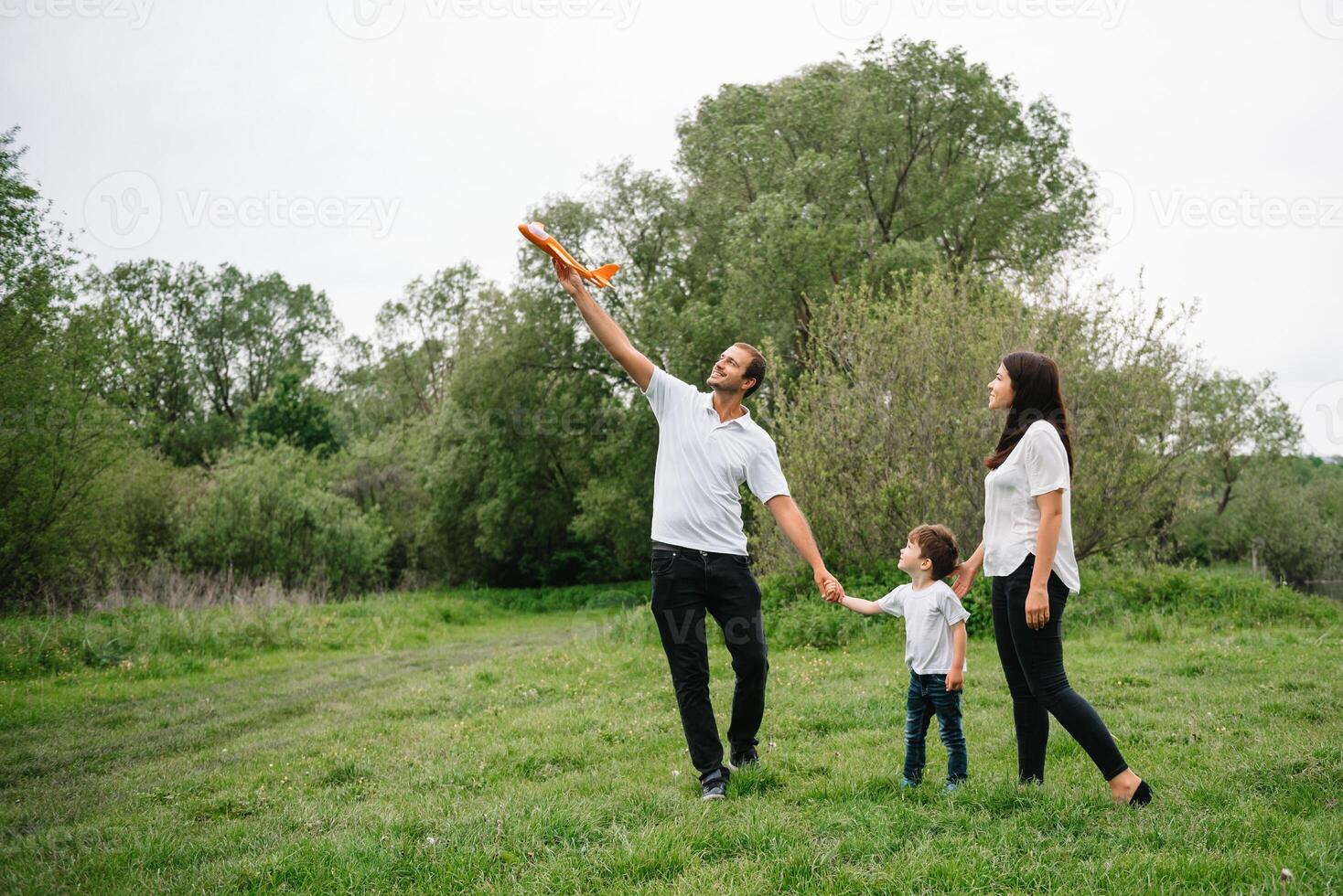 far, mor och son spelar med leksak flygplan i de parkera. vänlig familj. människor har roligt utomhus. bild tillverkad på de bakgrund av de parkera och blå himmel. begrepp av en Lycklig familj foto