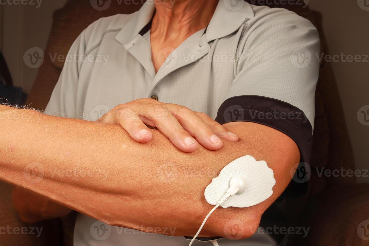 man använder sig av ett elektro terapi massager eller tiotals enhet på hans armbåge för smärta lättnad av muskler och gemensam foto