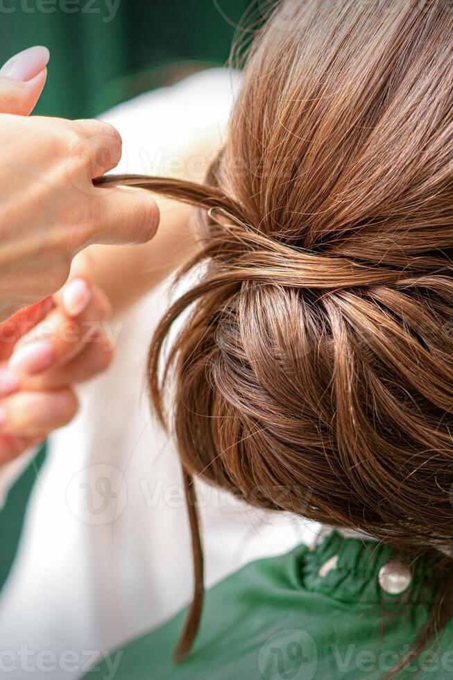 professionell frisör håller på med frisyr för en skön brunett ung kvinna med lång hår. begrepp av mode och skönhet. foto