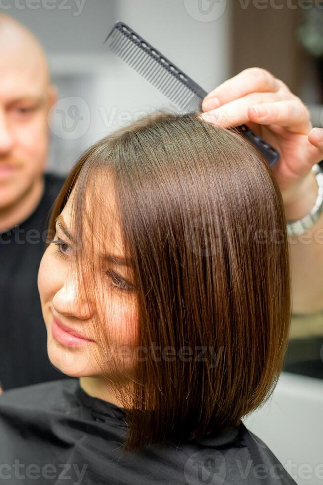 ung caucasian brunett kvinna har henne hårstyling förbi en manlig frisör på en salong. foto