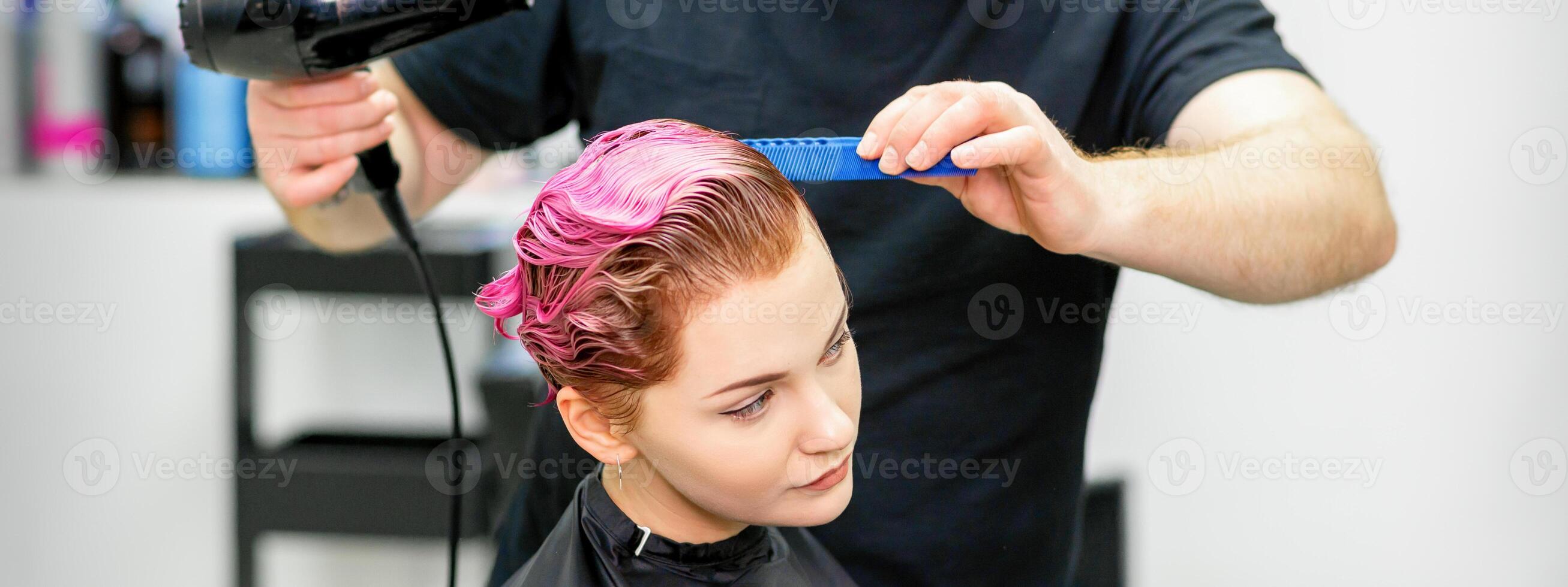 en frisör är torkning de rosa hår av de ung kvinna i en skönhet salong. foto