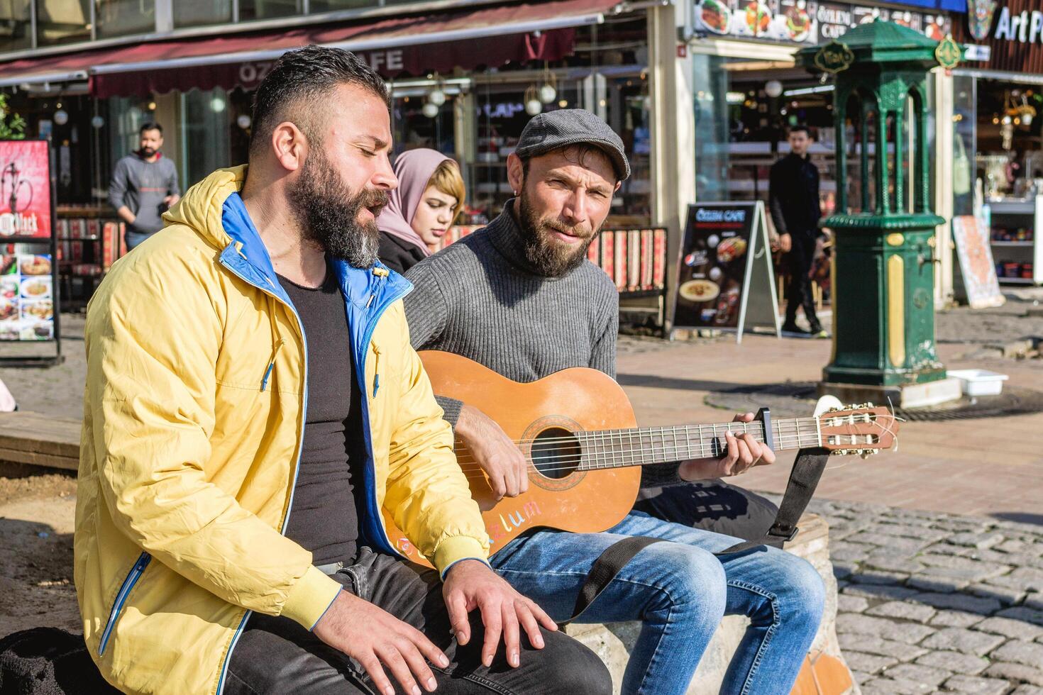 istanbul, Kalkon - december 29, 2022. två män är Sammanträde på bänk förbi de gata och ett av dem spelar gitarr. foto