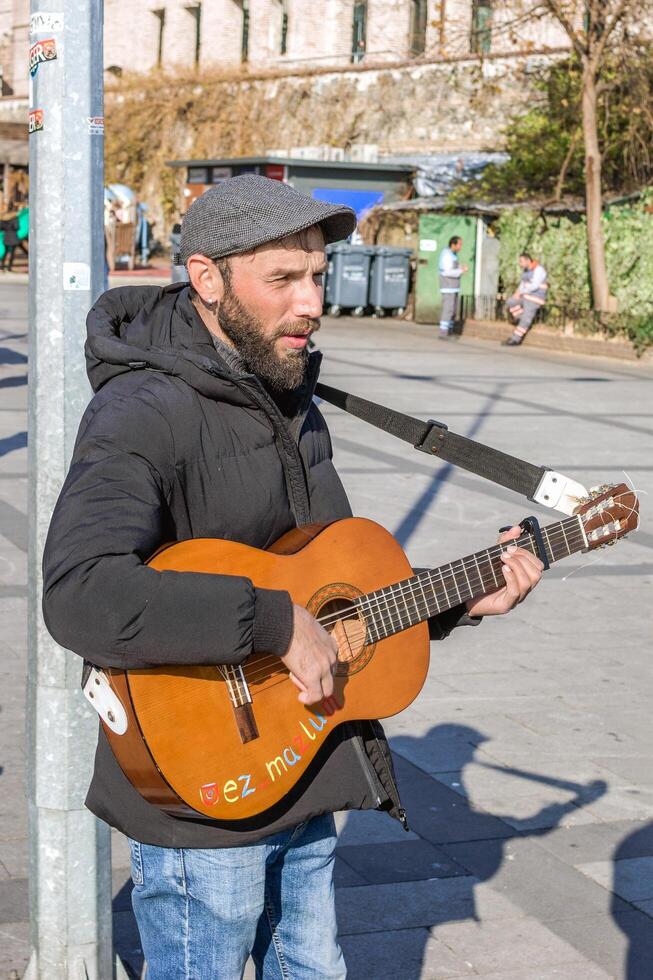 istanbul, Kalkon - december 29, 2023. fokuserade manlig gatumusikant klumpar hans gitarr på en stad gata hörn hoppas till tjäna några pengar. foto