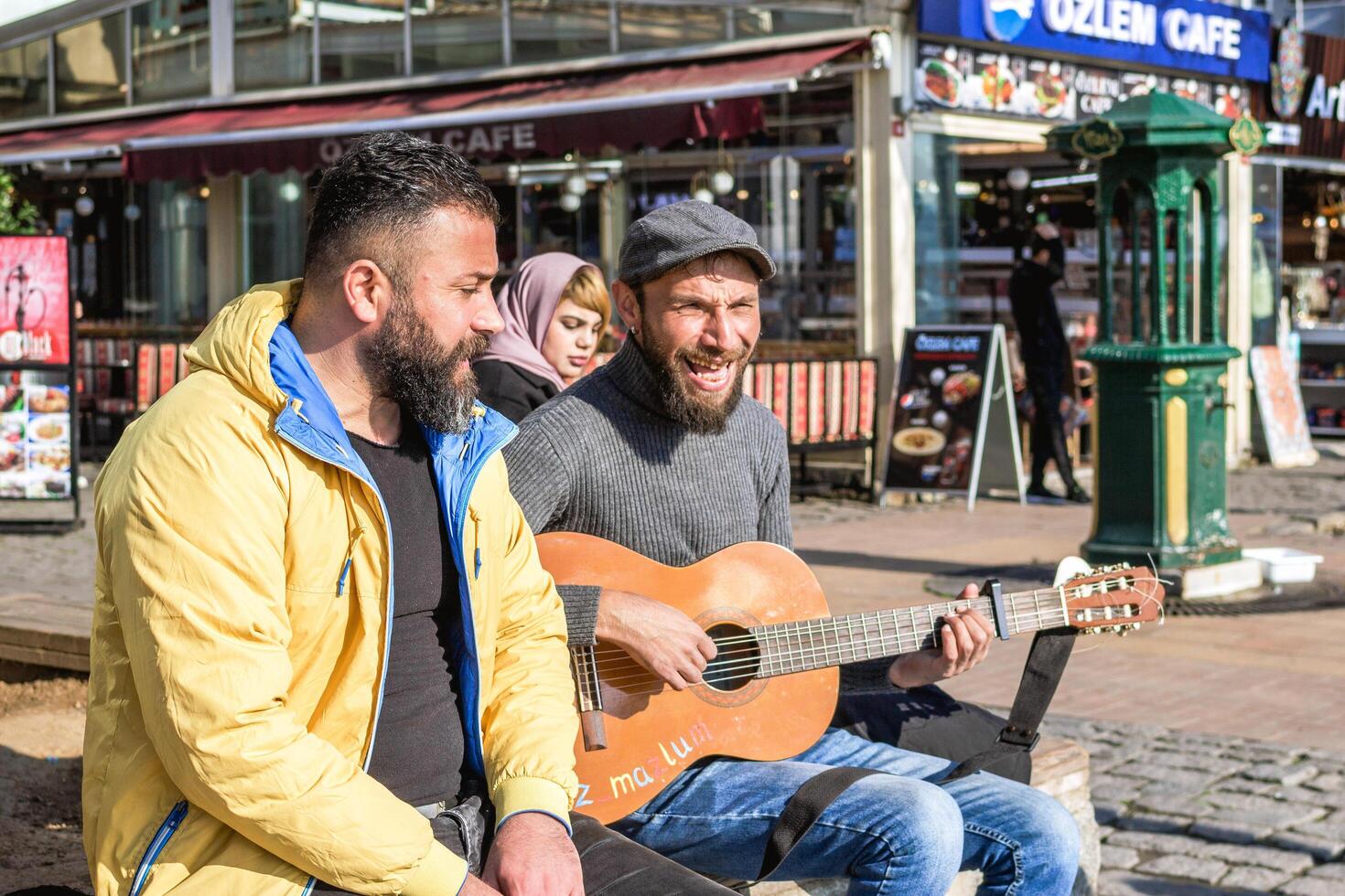 istanbul, Kalkon - december 29, 2022. två män, ett spelar gitarr och sång, de Övrig lyssnande spänt på en stad gata hörn. foto