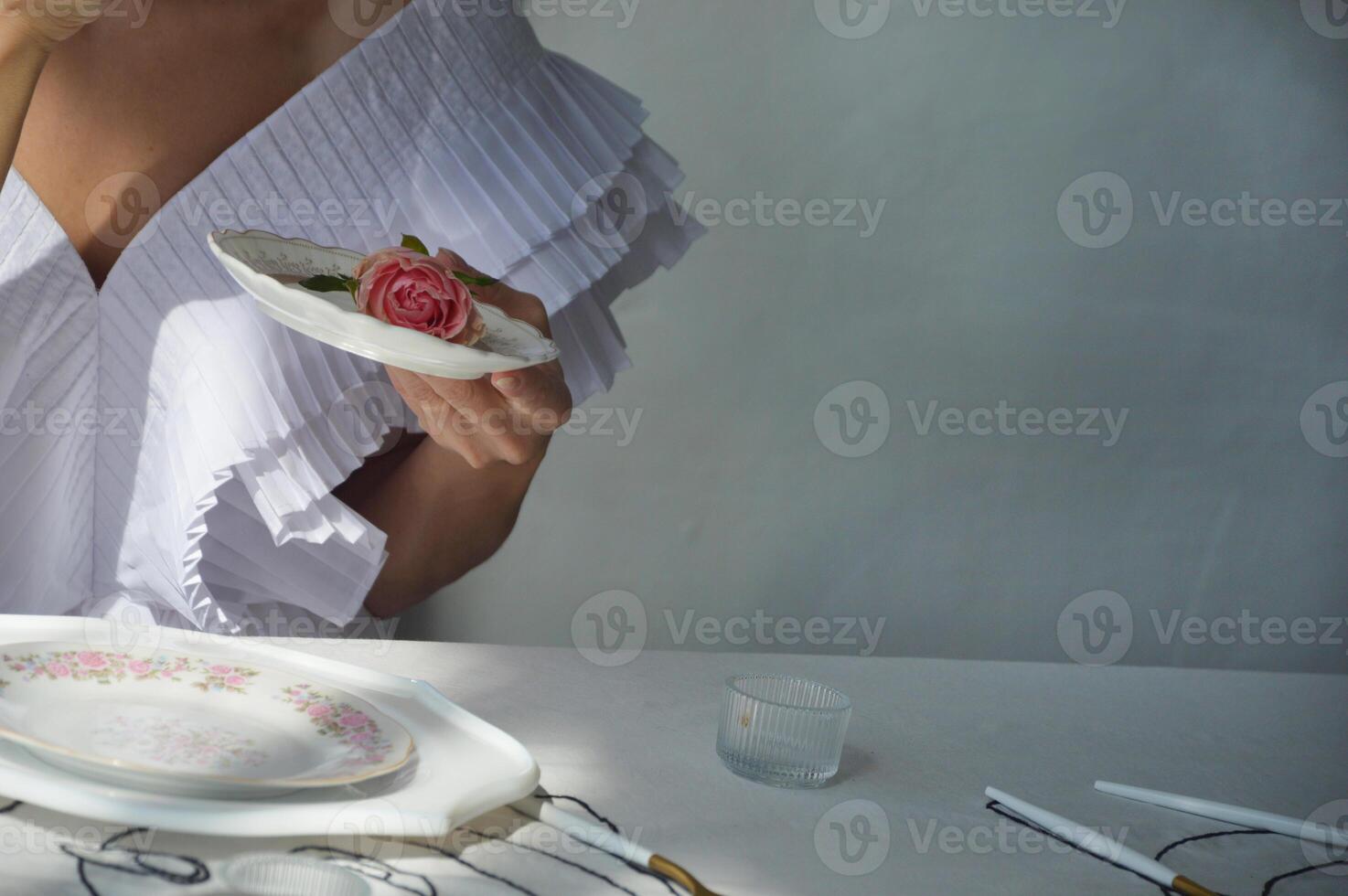 en kvinna, en flicka i en eleganta vit klänning innehar en vit porslin fat med en rosa reste sig i henne händer. te fest, morgon- av de brud. foto