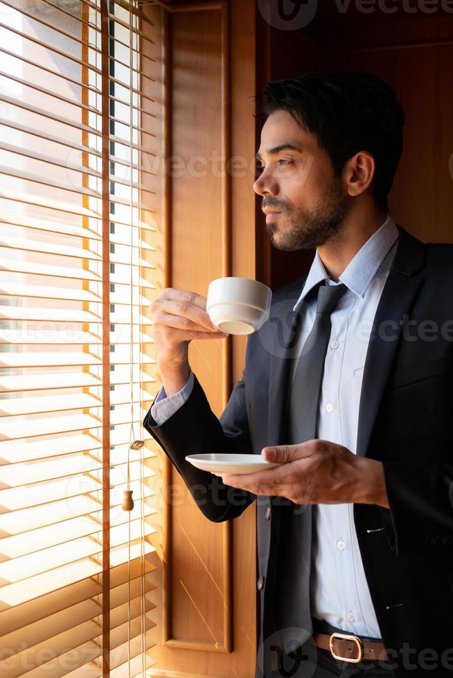 ung affärsman i Mellanöstern bär kostym och slips och dricker kaffe medan han tar en paus på kontoret. foto