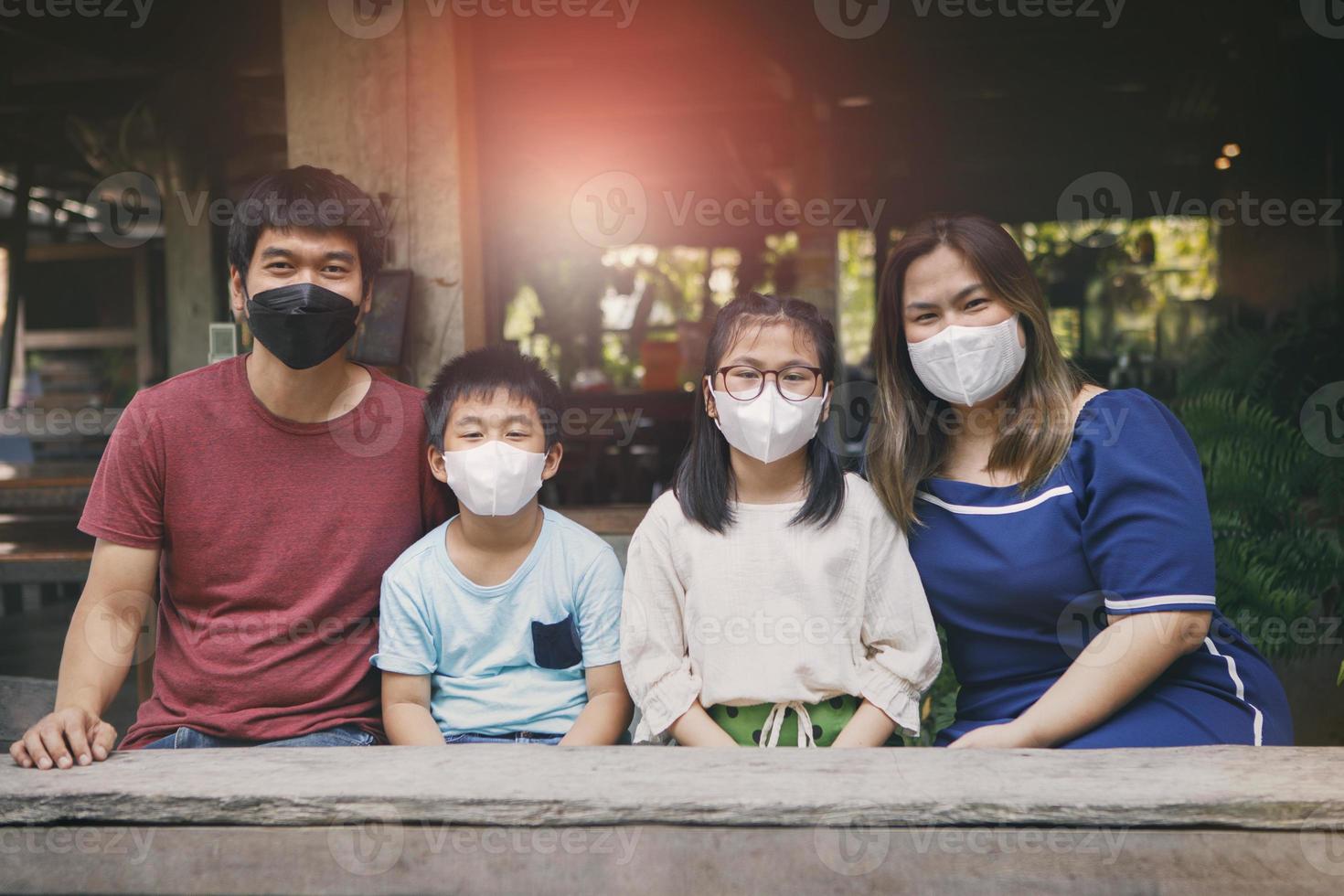 asiatisk familj som bär skyddsansiktsmask sitter i thailändska hem foto