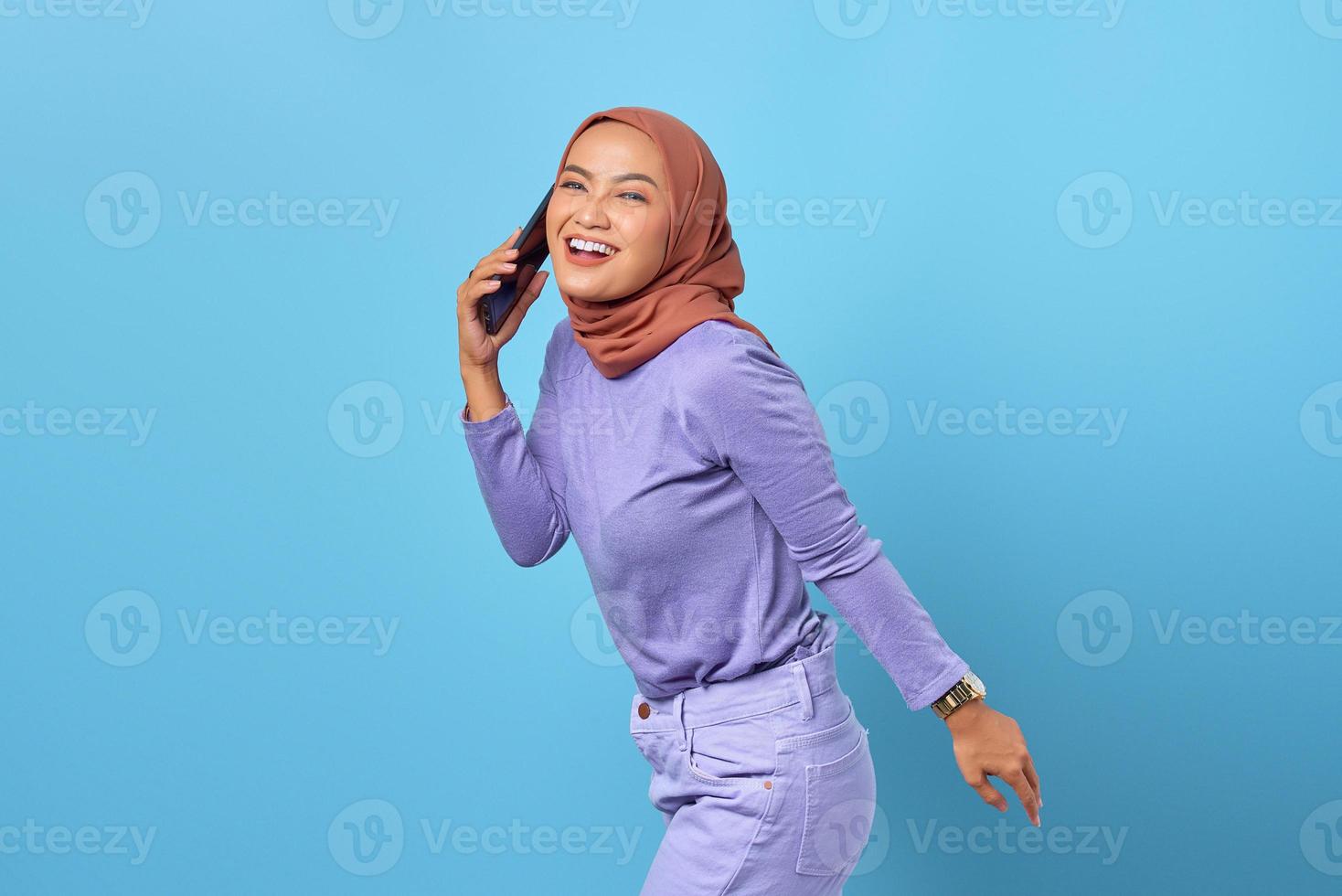 glad ung asiatisk kvinna pratar i en mobiltelefon med sin pojkvän isolerad på blå bakgrund foto