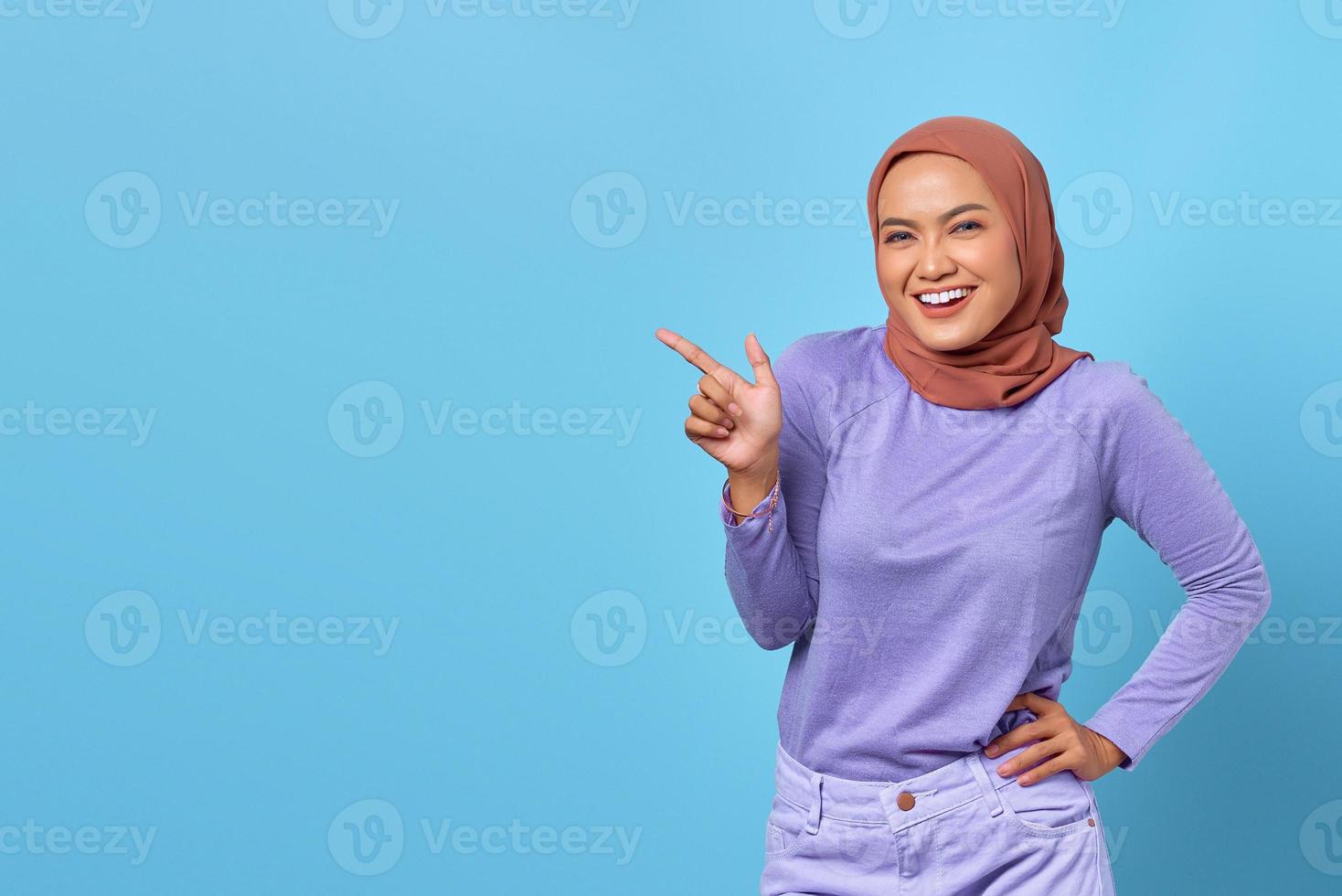 porträtt av leende ung asiatisk kvinna pekar finger på kopia utrymme på blå bakgrund foto