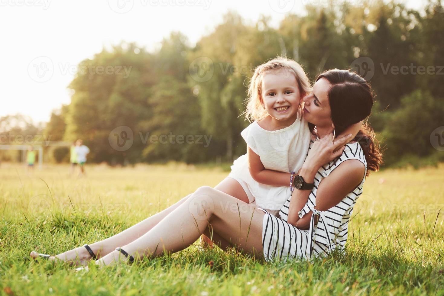 glad mor och dotter kramas i en park i solen på en ljus sommarbakgrund av örter. foto