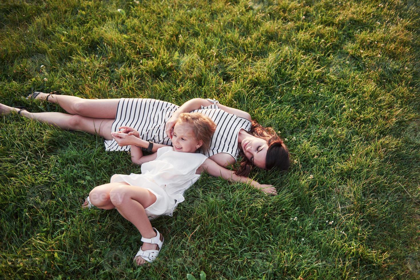 glad liten flicka och hennes mamma ha kul utomhus på det gröna gräset i solig sommardag. foto