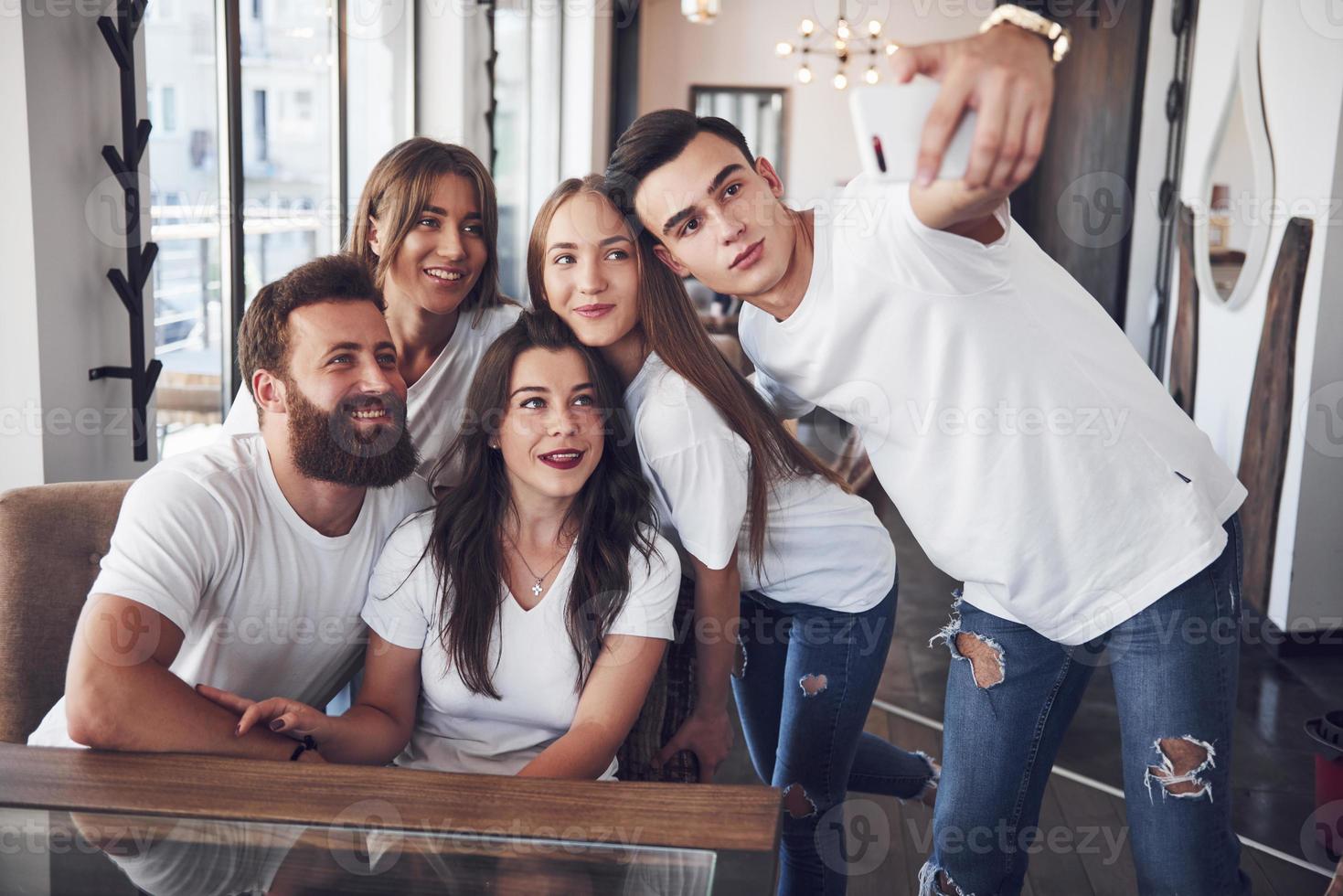 en grupp människor gör ett selfiefoto på ett kafé. de bästa vännerna samlades vid ett middagsbord och åt pizza och sjöng olika drinkar foto