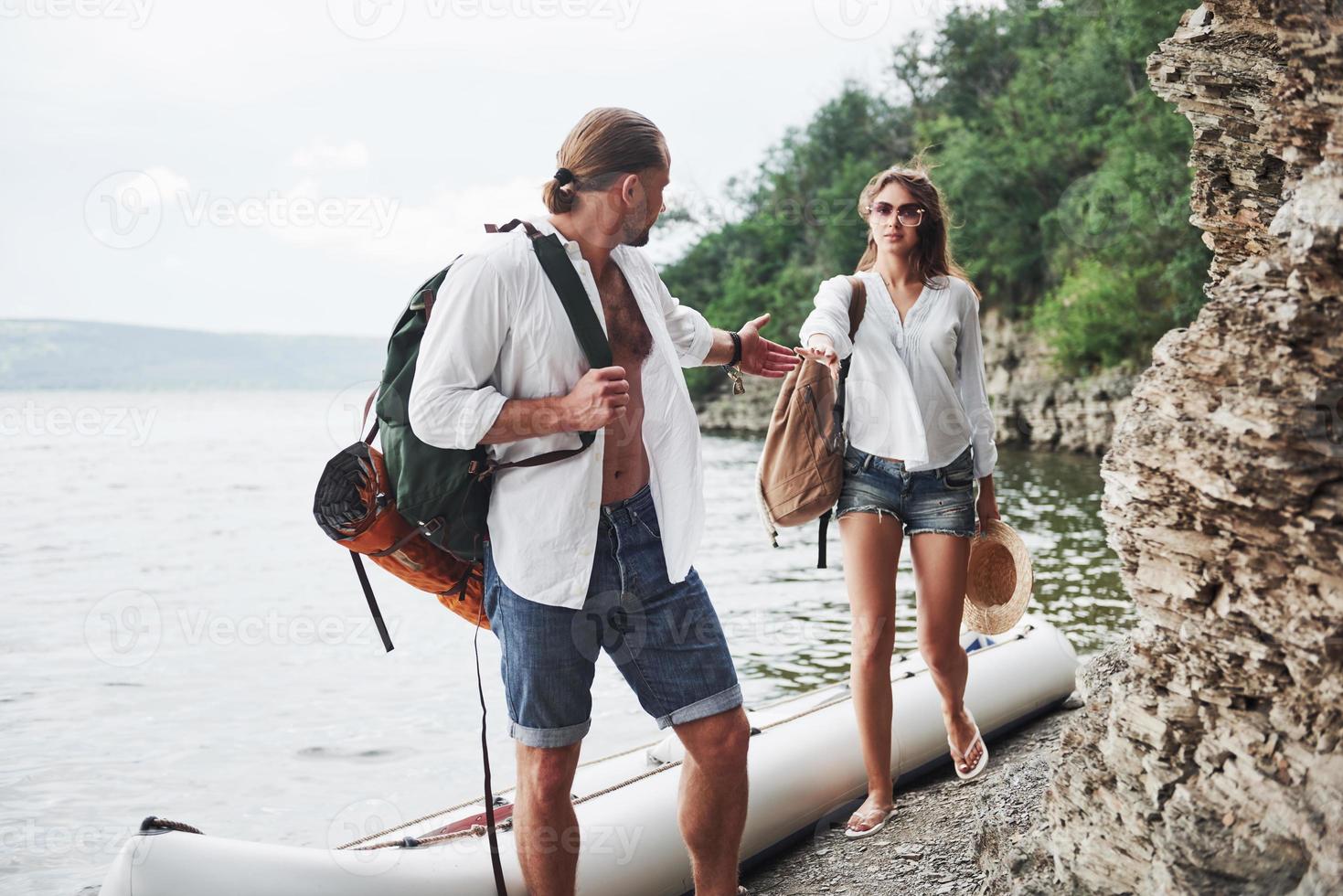 söta unga och par på floden bakgrund. en kille och en tjej med ryggsäckar reser med båt. resenär sommar koncept foto
