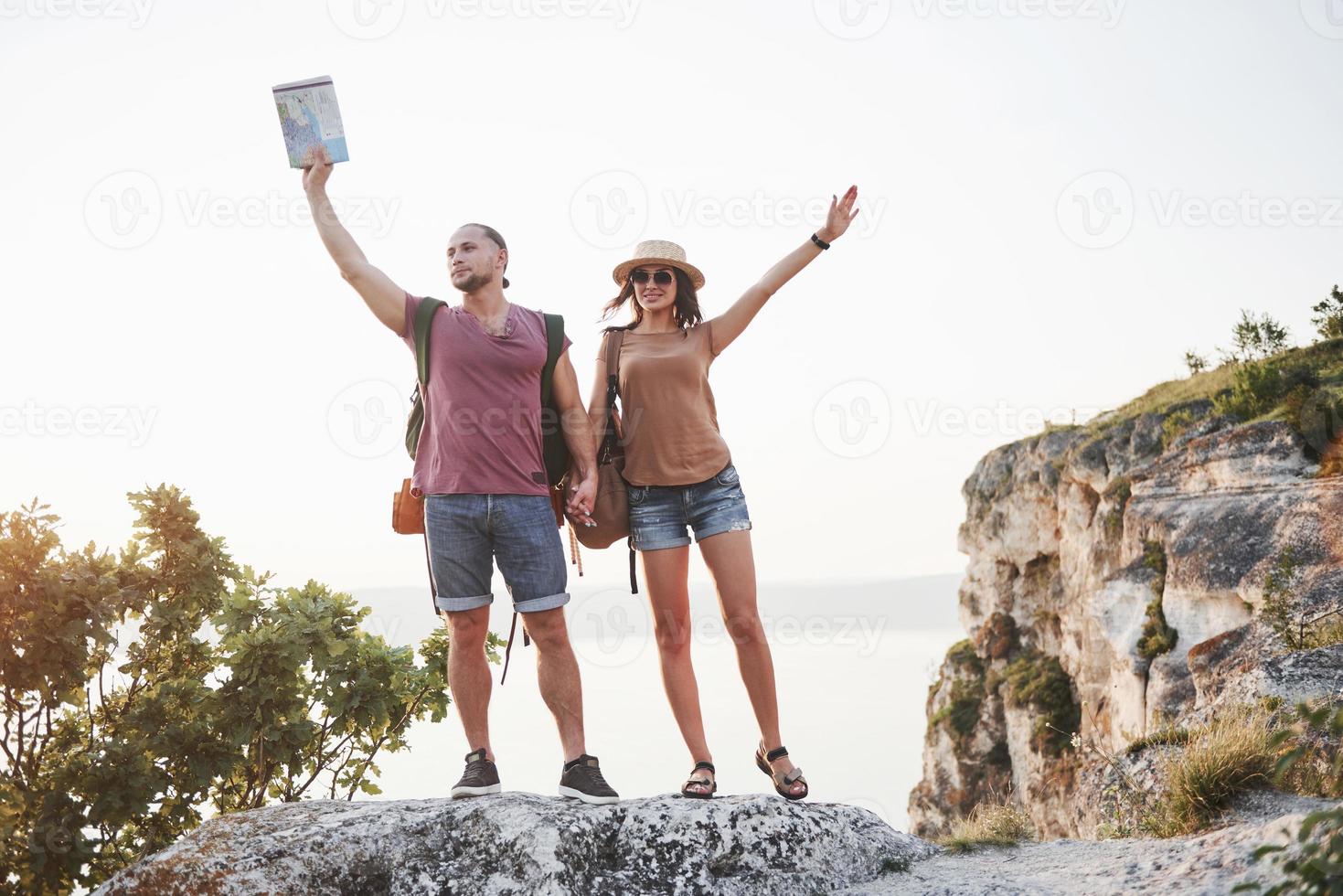 två turist man och kvinna med ryggsäckar står på toppen av klippan och njuter av soluppgången. resande berg och kust, frihet och aktivt livsstilskoncept foto