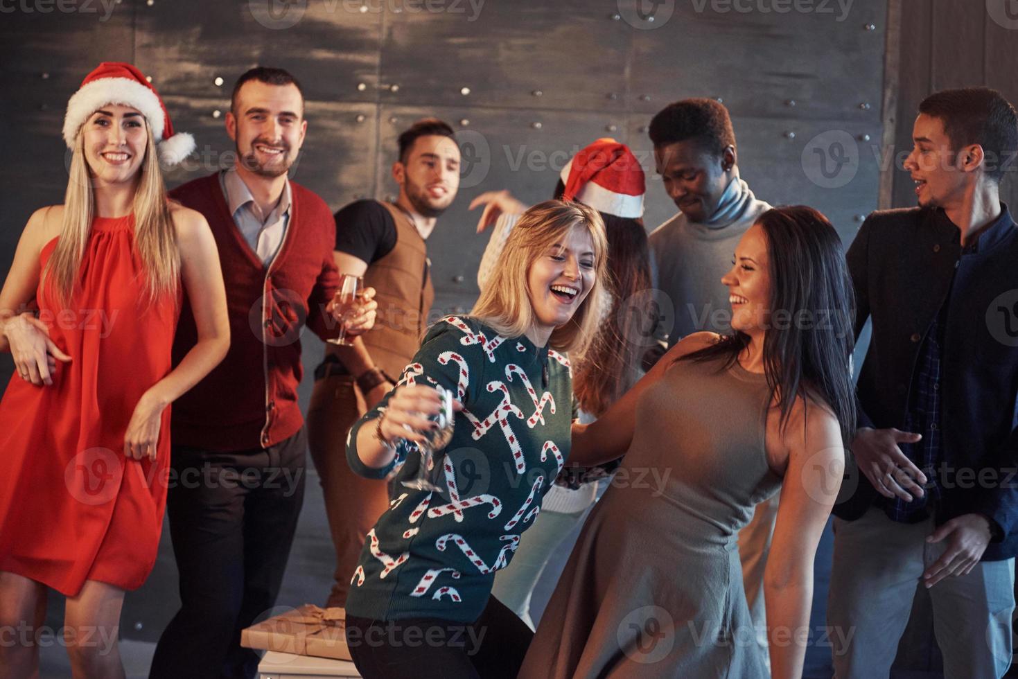 festa med vänner. de älskar julen. grupp glada ungdomar som bär tomtebloss och champagneflöjter som dansar i nyårsfest och ser glada ut. begrepp om samhörighetslivsstil foto