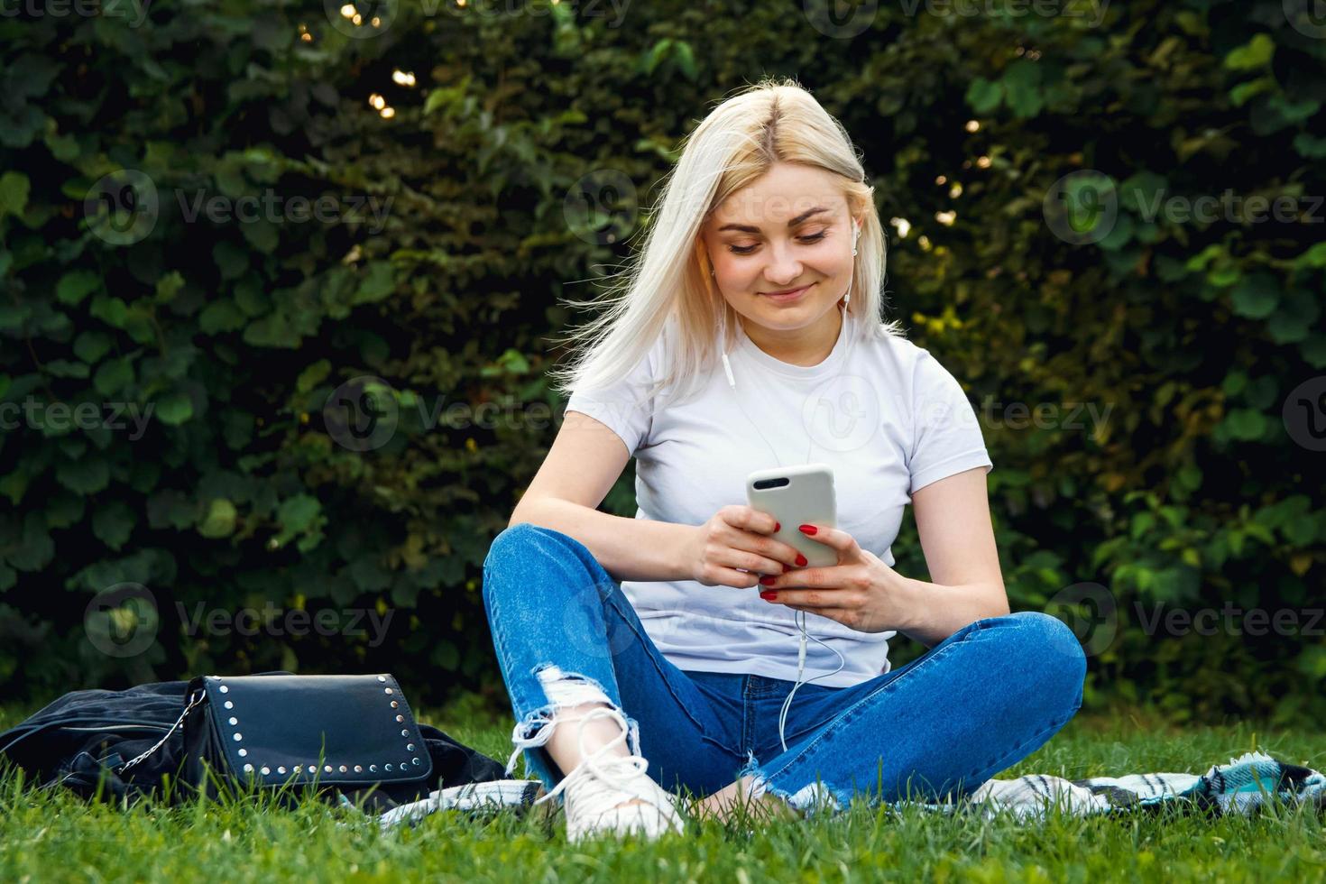 kvinna i hörlurar och smartphone i händer sitter på grönt gräs foto