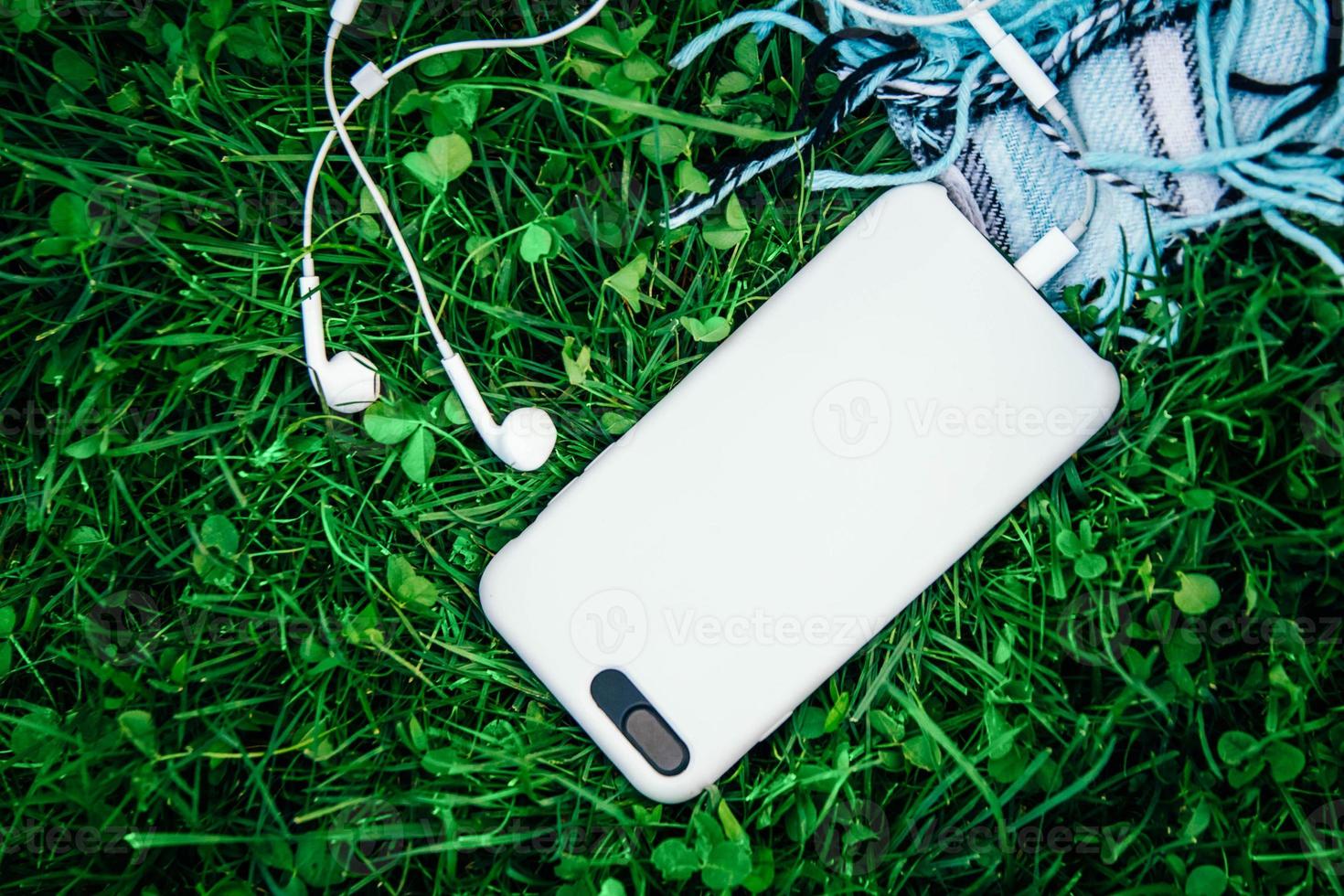 vita hörlurar och vit smartphone på grönt gräs foto