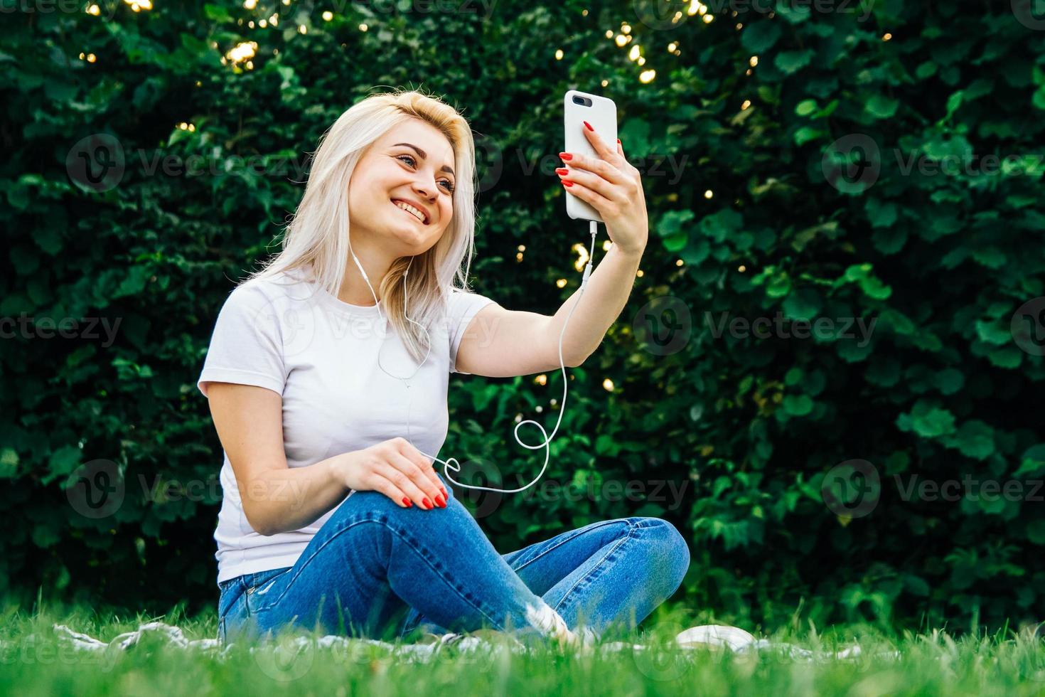 kvinna i hörlurar och smartphone på grönt gräs foto