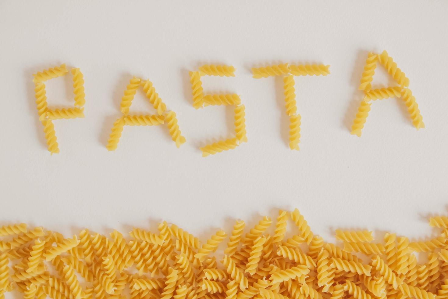 inskription pasta på vit bakgrund och spiral pasta foto