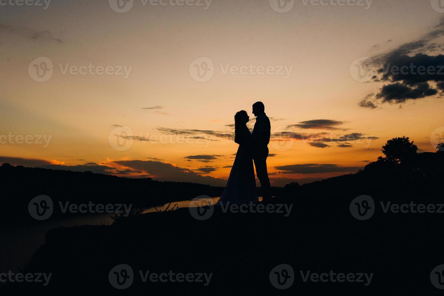 silhuetter av en lycklig ung par kille och flicka på en bakgrund av orange solnedgång foto