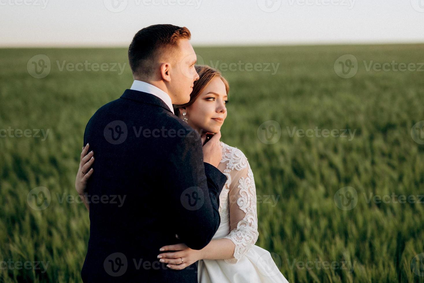 brudgummen och bruden går längs det vetegröna fältet foto