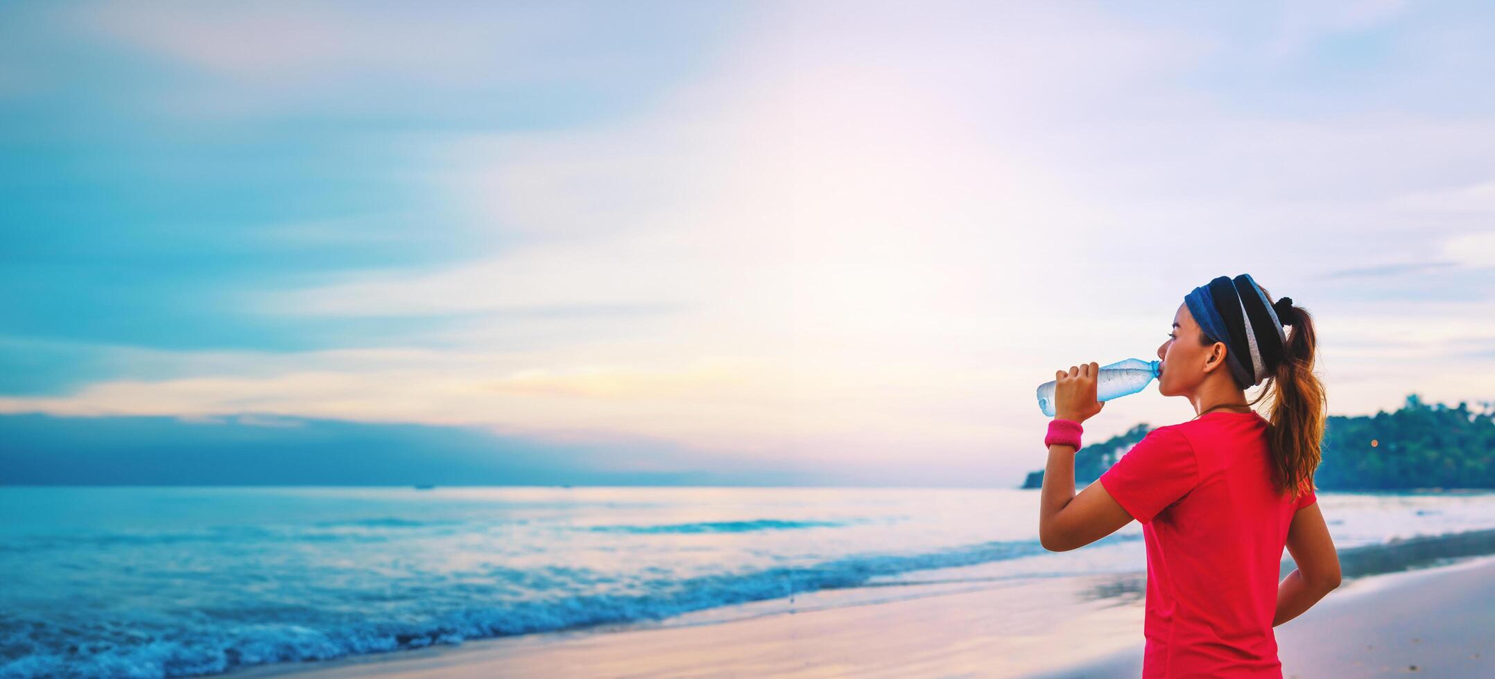 asiatiska kvinnor jogging träning på stranden på morgonen. koppla av med havspromenaden och dricksvatten från plastflaskorna foto