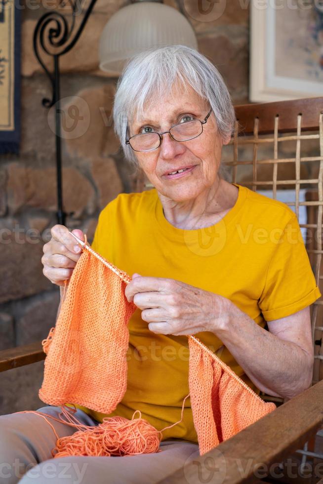 70-talsmormor tittar på kameran och njuter av att sticka hemma. foto