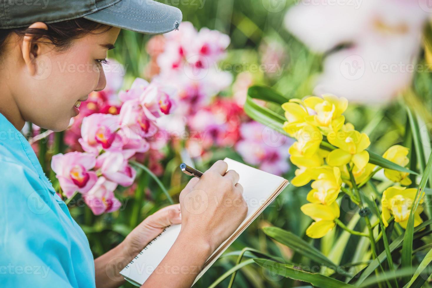 unga kvinnor skriver anteckning bland orkidé trädgård. färgglada orkidéer, orkidé blomma. foto